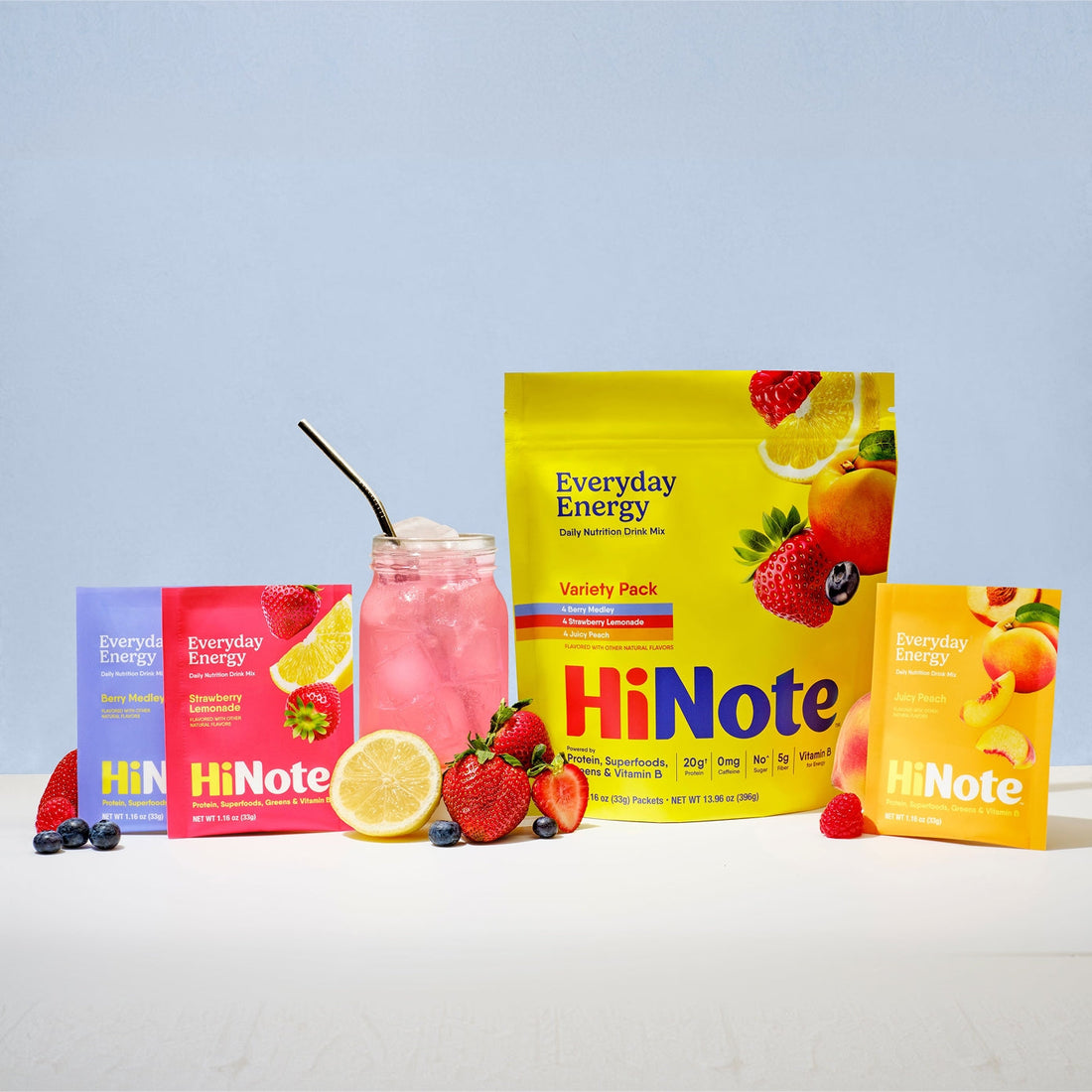 Front facing HiNote Everyday Energy variety pouch and packets with pink drink and fresh berries on light blue background