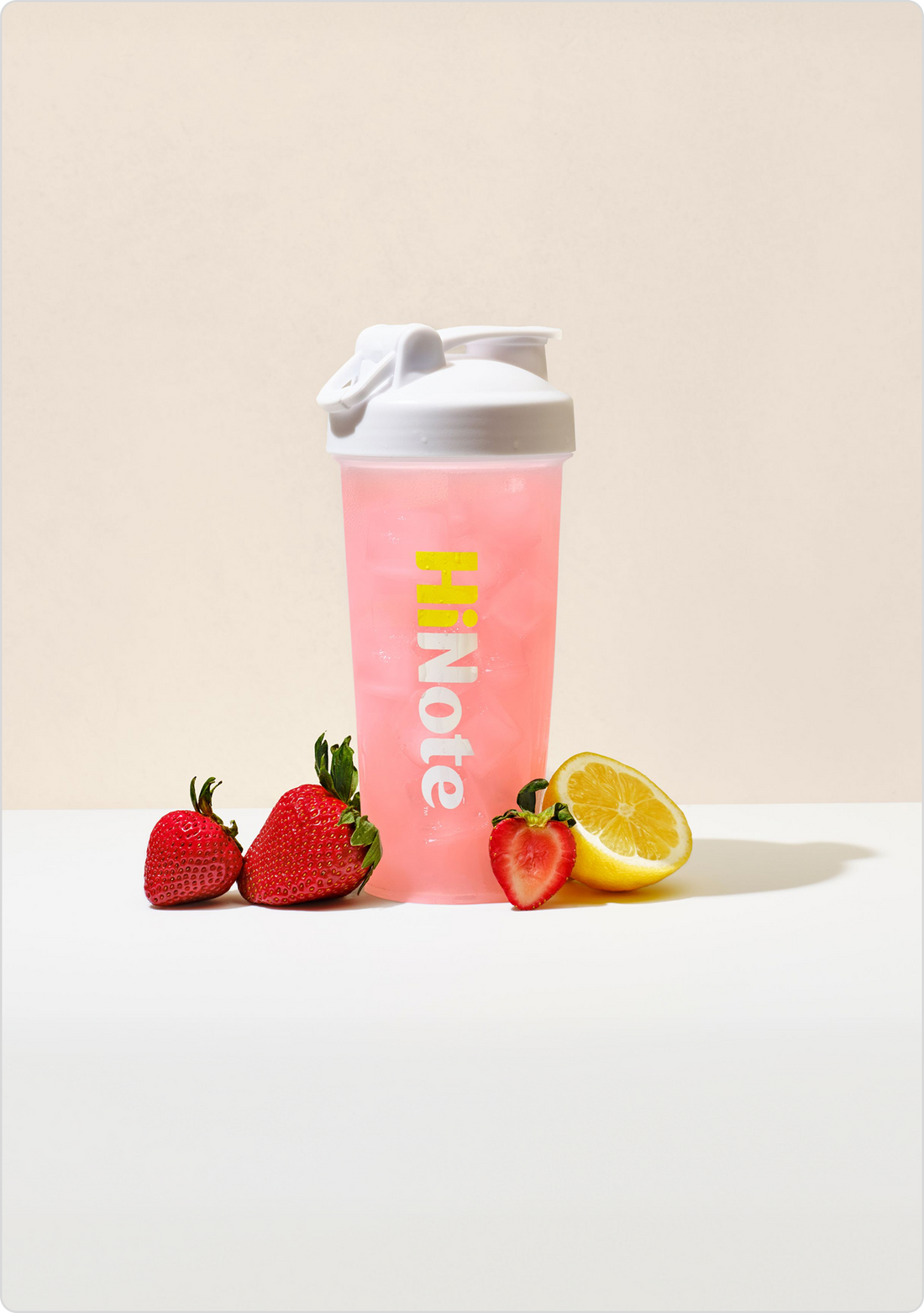 Front HiNote pink shaker bottle with white flip lid, vertical logo, iced drink and strawberries and lemon on white background
