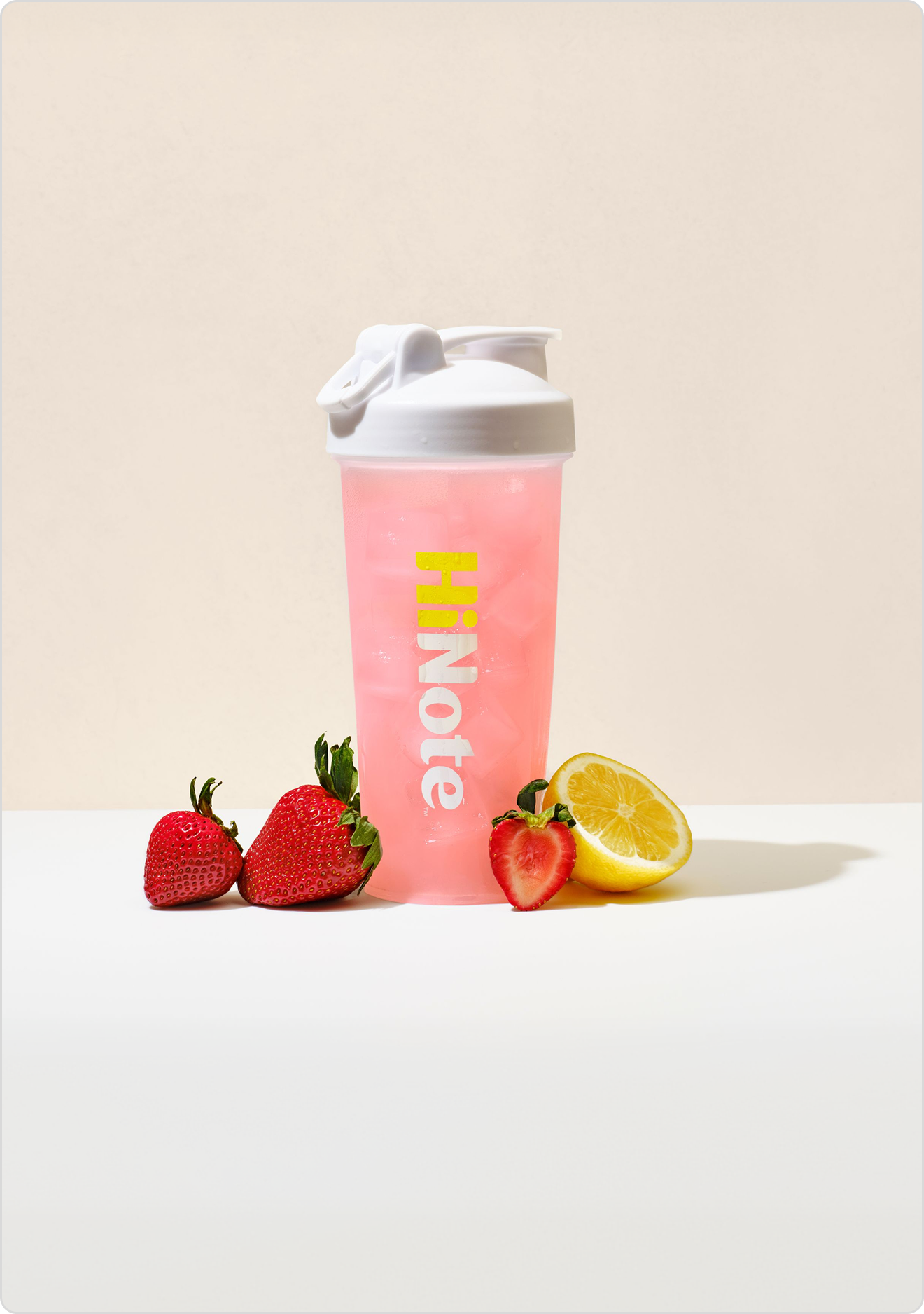 Front HiNote pink shaker bottle with white flip lid, vertical logo, iced drink and strawberries and lemon on white background