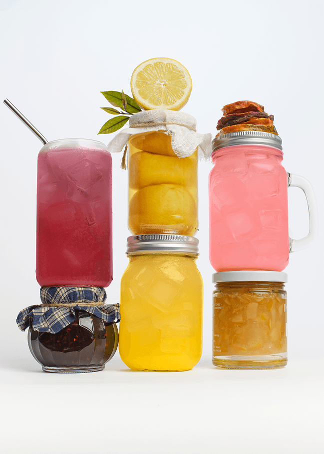 Stack of glass jars with colorful drinks and garnishes on a white background
