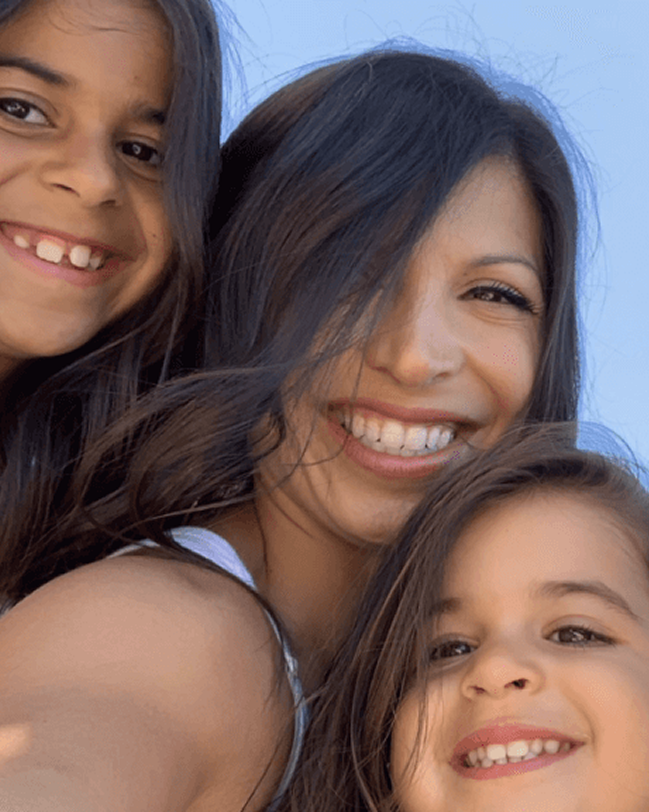 Woman taking a close-up selfie with two smiling girls against a clear blue sky