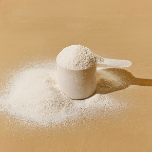 Close-up of scoop of collagen peptide powder showing fine white texture on a tan background