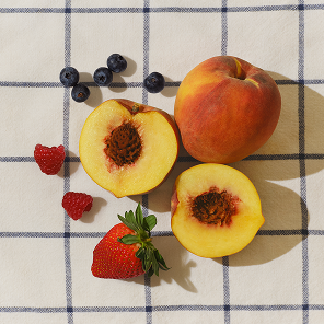 Top-down view of fruit blend with halved peaches, strawberry, raspberries, and blueberries on a blue-and-white checkered cloth