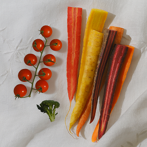 Top-down view of colorful carrots, cherry tomatoes, and broccoli representing a vegetable phytonutrient blend on white cloth