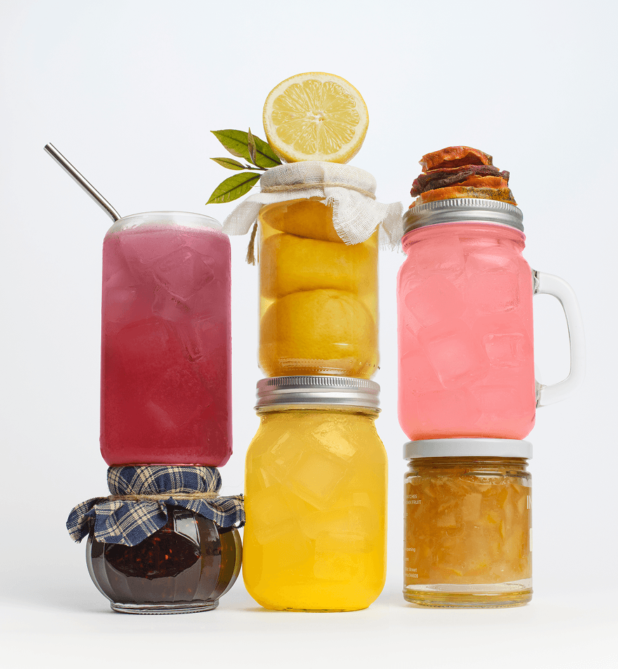 Front view of three stacked mason jars showcasing colorful iced drinks and preserved fruit on a white background